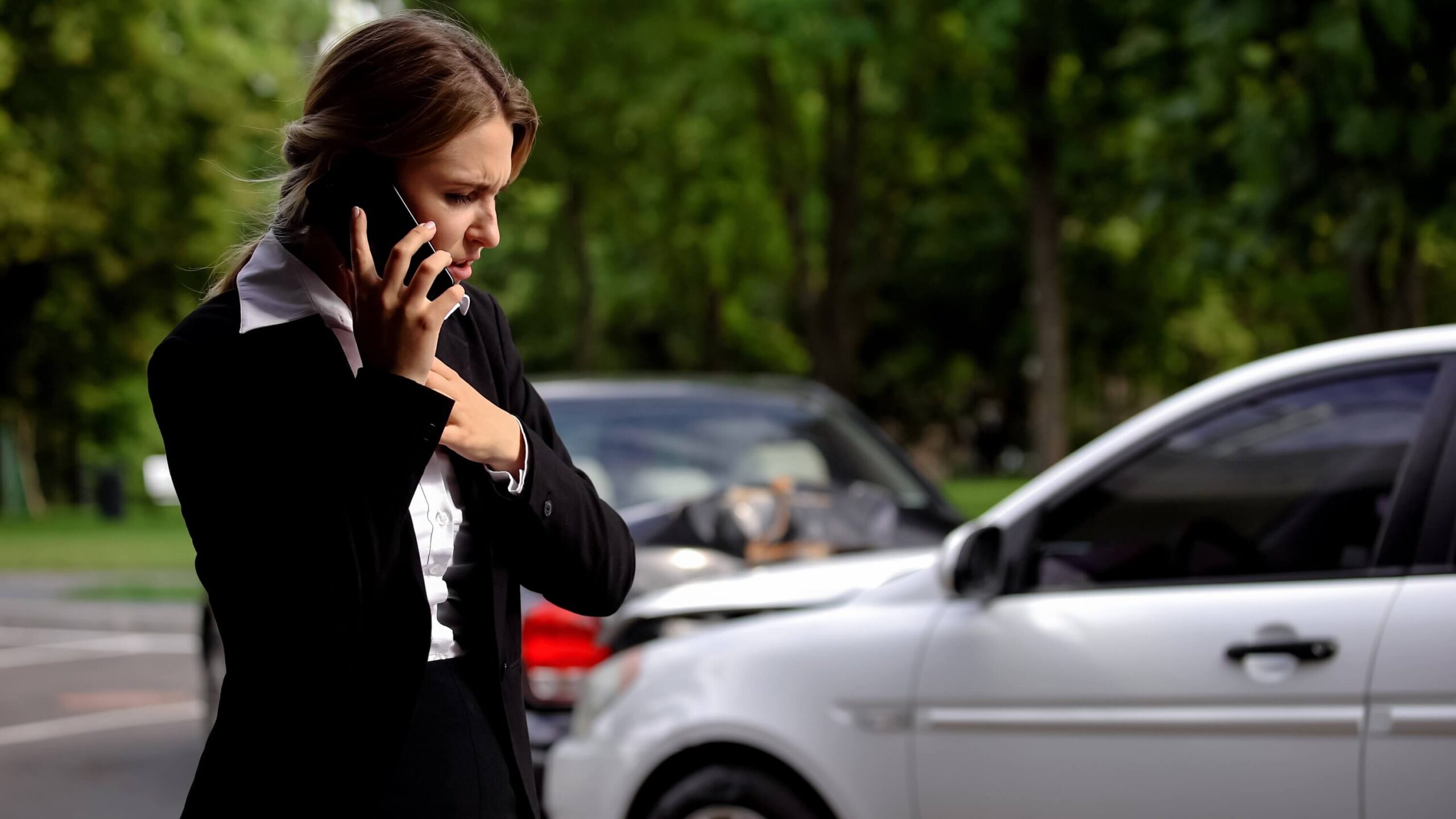 Stressed female driver talking on phone truck collision scene, car damage, insurance