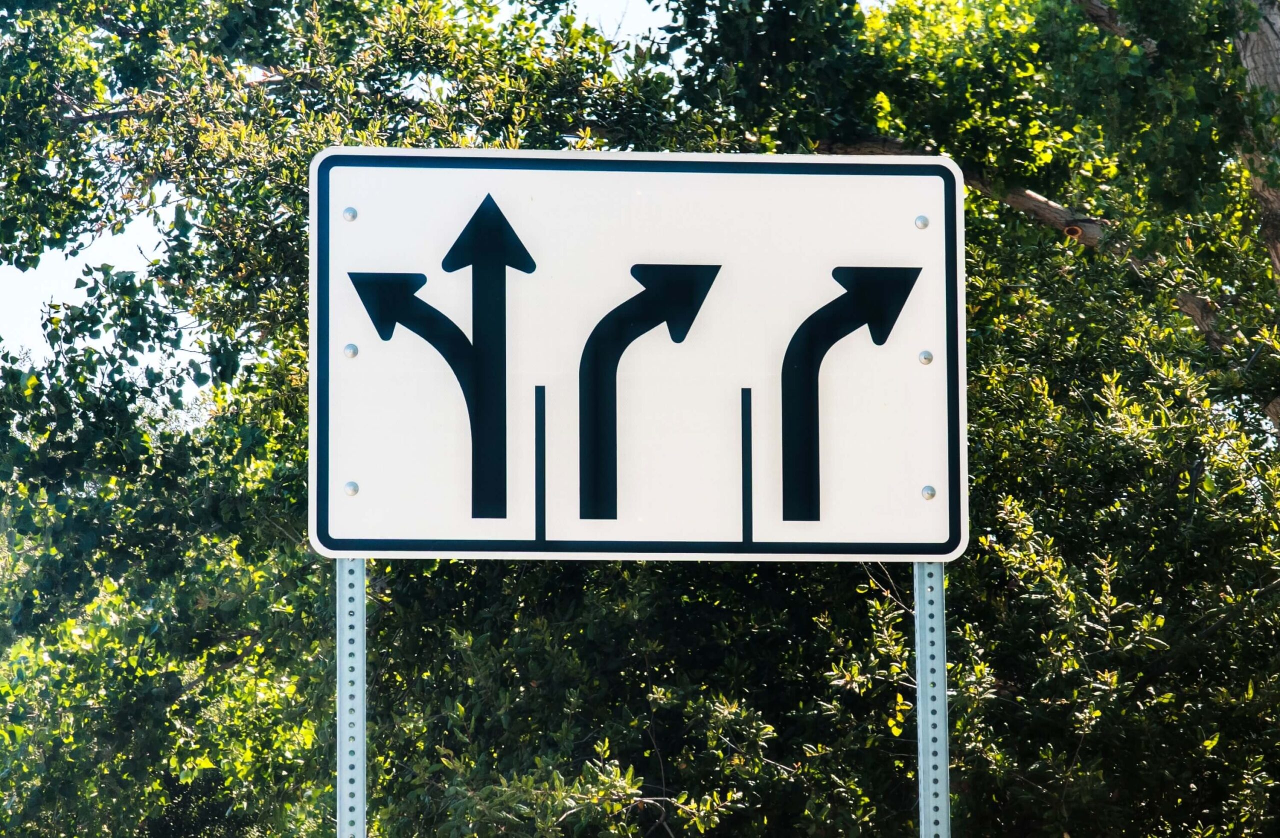 A white traffic sign with black arrows informing drivers of left, straight and right turn lanes