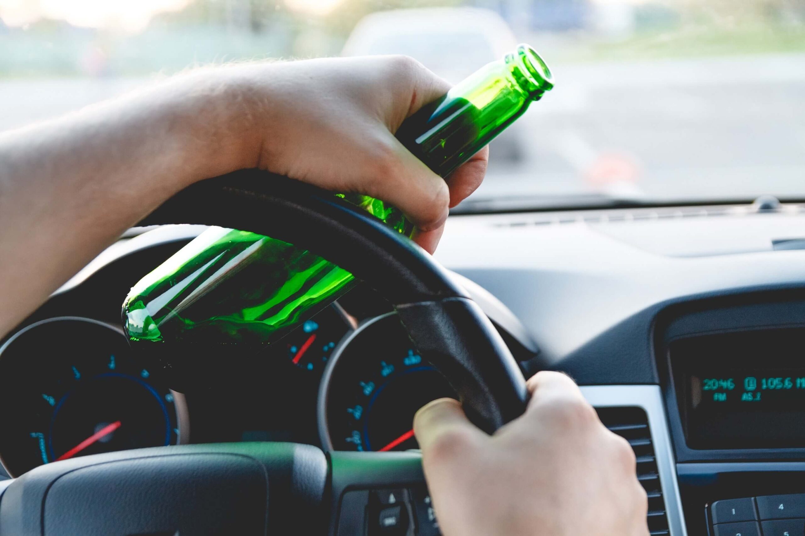 Drunk young man driving a truck with a bottle of beer